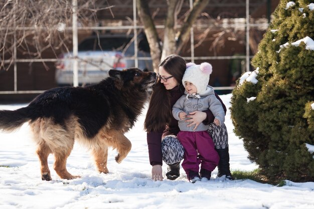 Mãe e filha caminhando em um dia de inverno e brincando com seu cachorro