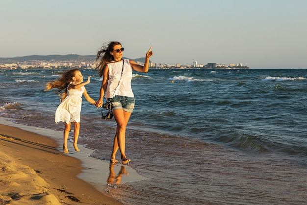 Mãe e filha caminhando na praia em uma noite ensolarada de verão