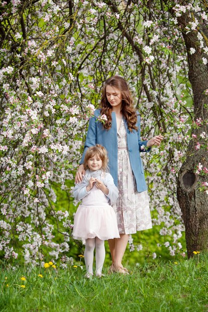 Mãe e filha caminhando no jardim de maçã florescendo. mamãe ama seu filho. história de primavera. família feliz em lindo dia de primavera