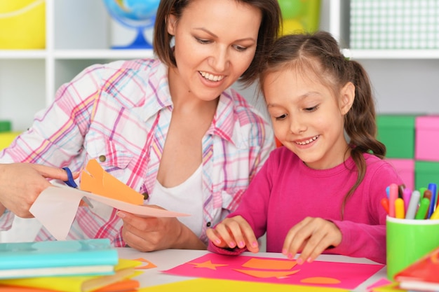 Mãe e filha colando e cortando papel para cartão