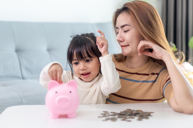 Mãe e filha colocando moedas no cofrinho. Orçamento familiar e conceito de economia. Conceito de conta poupança júnior