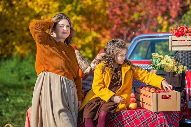 Mãe e filha com cestos de legumes no fundo da natureza do outono ao lado de um carro retrô vermelho