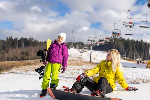 Mãe e filha com pranchas de snowboard em resort de inverno