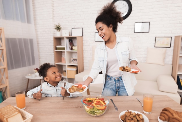 Mãe e filha comem juntos na cozinha.