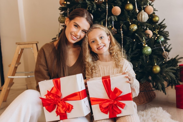 Mãe e filha comemoram o Natal com presentes ao lado da árvore