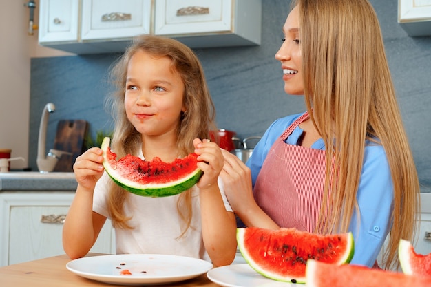 Mãe e filha comendo melancia em casa na cozinha