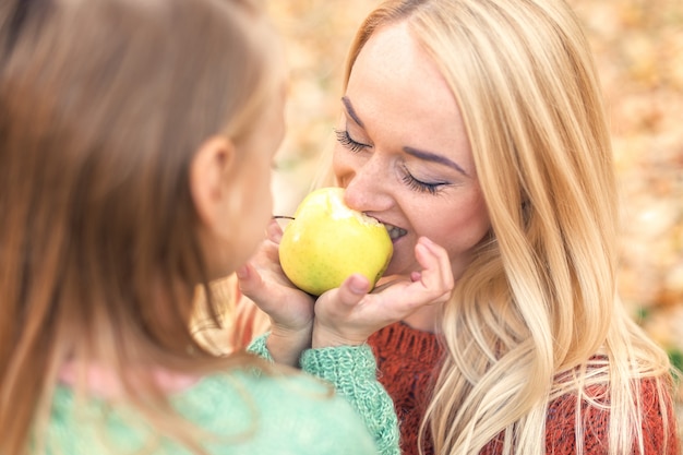 Mãe e filha comendo uma maçã no parque outono.