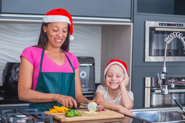 Mãe e filha cozinhando para a ceia de natal. mãe e filha com chapéu de papai noel cozinhando