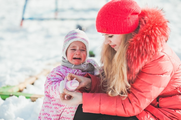 Mãe e filha criança caminhando em um parque de inverno. A menina está tocando a neve pela primeira vez, grande decepção