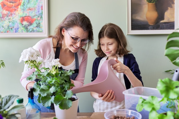 Mãe e filha criança juntos cuidam de plantas de interior em vasos, menina regando a flor do regador. Hobbies e lazer, cuidado, família, planta de casa, conceito de amigos em vasos domésticos