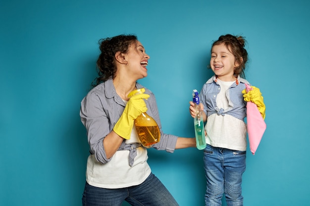 Mãe e filha curtindo o tempo juntas durante o trabalho de casa, em pé contra o azul e rindo alegremente