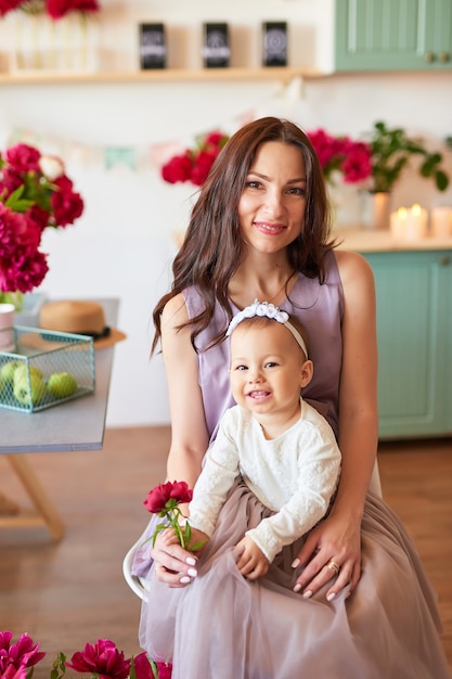 Mãe e filha da família com flores de peônias na cozinha em casa. Feliz mãe e filha. Família feliz.