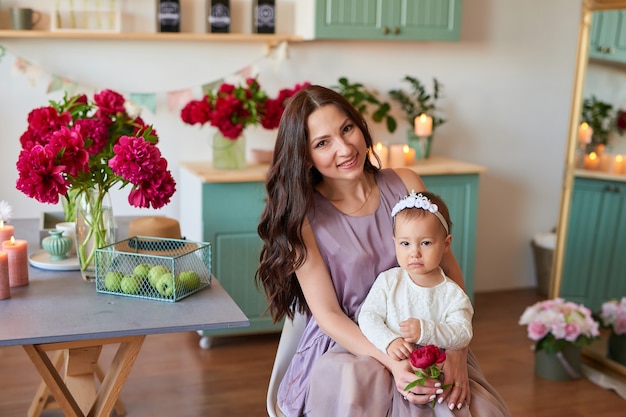 Mãe e filha da família com flores de peônias na cozinha em casa. Feliz mãe e filha. Família feliz.