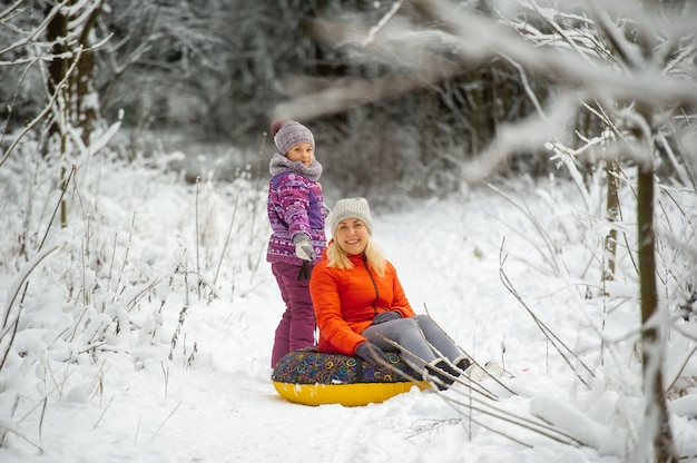 Mãe e filha da família no inverno com um círculo inflável caminham pela floresta coberta de neve