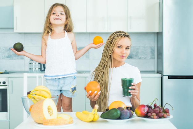 Mãe e filha de crescimento saudável da criança misturando coquetel com frutas mãe e filha bebendo