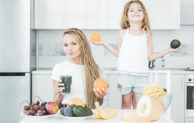 Mãe e filha de crescimento saudável da criança misturando coquetel com frutas mãe e filha bebendo