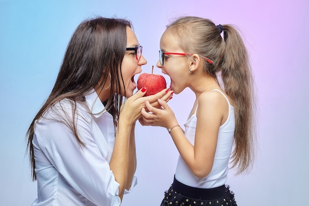 Mãe e filha de óculos, mordendo uma grande maçã vermelha.