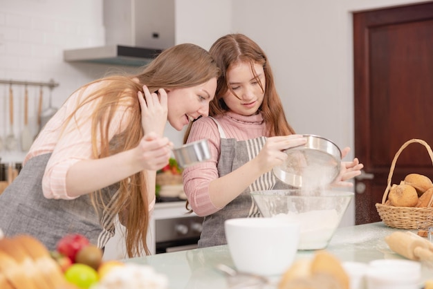 Mãe e filha de seus filhos mais novos em uma área de cozinha moderna celebrando a alegre aprendizagem decoração de bolos de bolo filha pequena feliz prepara bolos doces com mãe carinhosa no fim de semana em casa