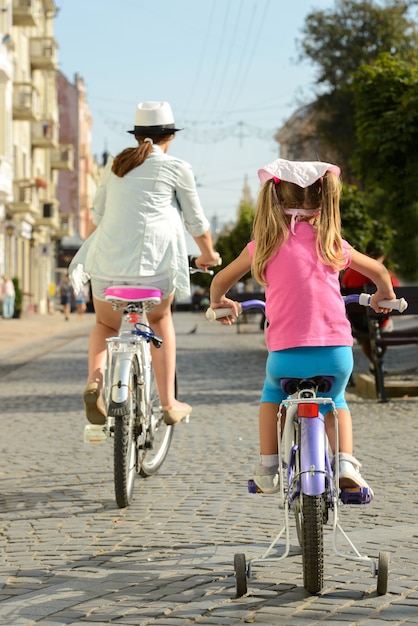 Foto mãe e filha de sorriso bonitas que montam uma bicicleta.