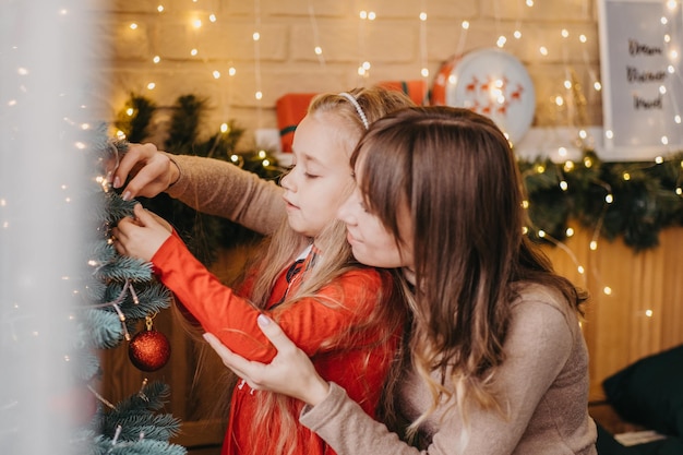 Mãe e filha decoram a árvore de natal juntas. paternidade tradicional.