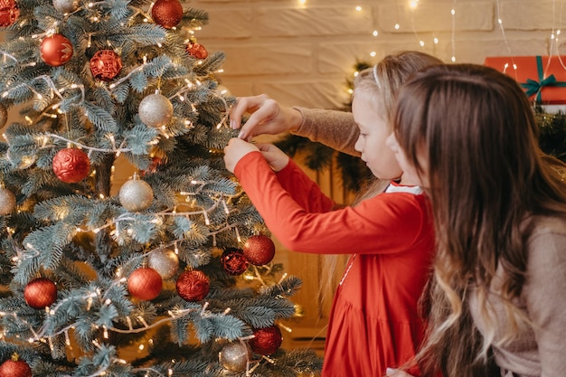 Mãe e filha decoram a árvore de natal juntas. paternidade tradicional.