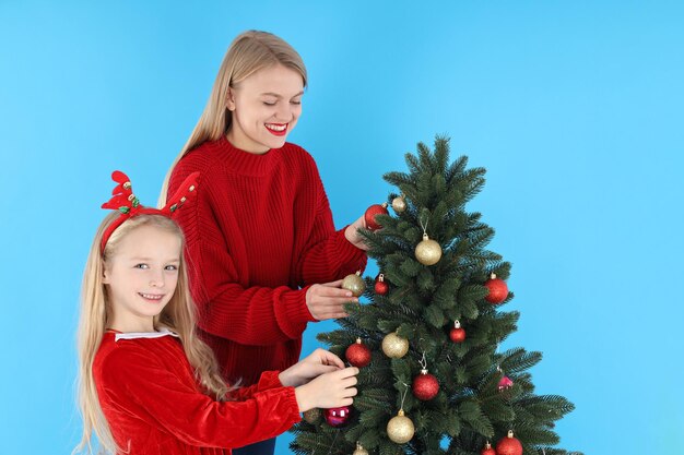 Mãe e filha decoram árvore de natal em fundo azul