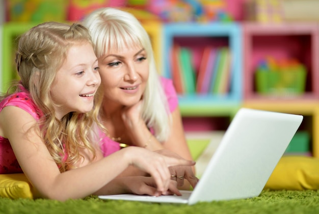 Mãe e filha deitadas no chão e usando laptop