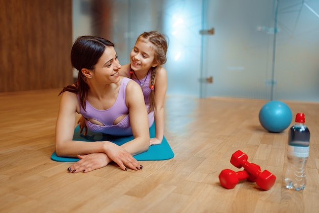 Mãe e filha deitados juntos na esteira no ginásio, treino de fitness, ginástica.