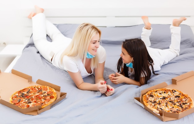 Mãe e filha deitam-se na cama em casa com pizza durante a quarentena, quarentena de lazer
