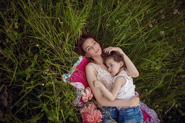 Foto mãe e filha deitam-se num campo verde no verão e relaxam ao sol