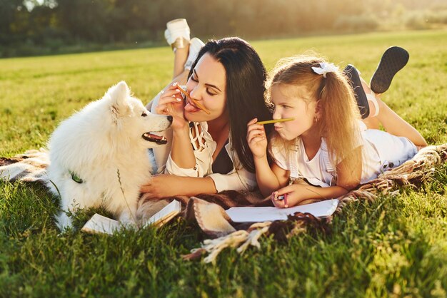 Mãe e filha descansam enquanto se deitam na grama com seu cachorro fofo