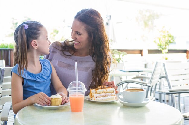 Mãe e filha desfrutando bolos no terraço do café