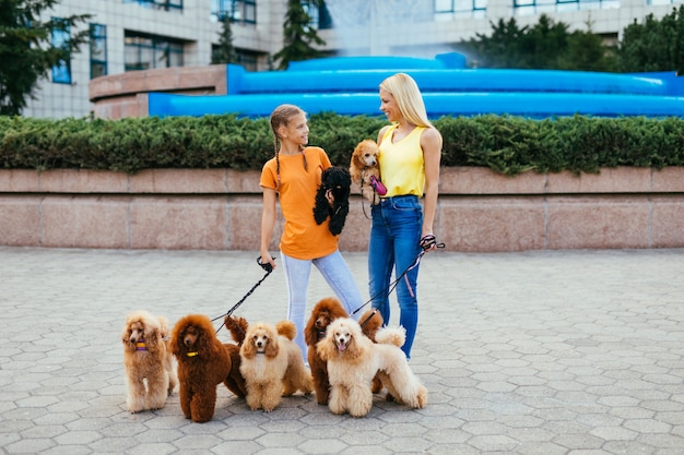 Mãe e filha desfrutando de passeio junto com seus poodles na rua da cidade.