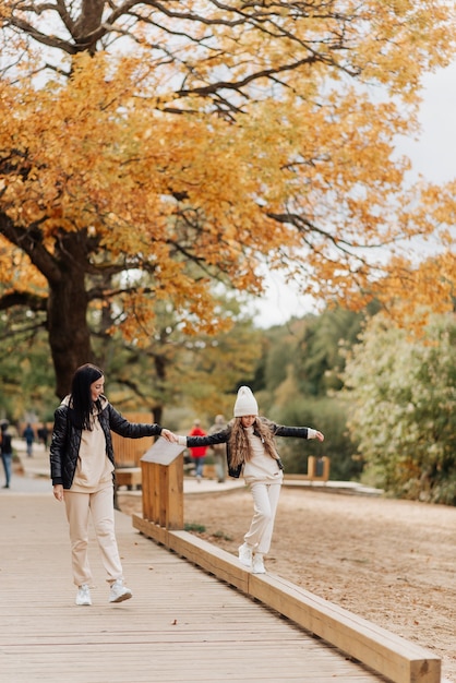 Mãe e filha elegantes em jaquetas de couro caminham juntas no parque de outono