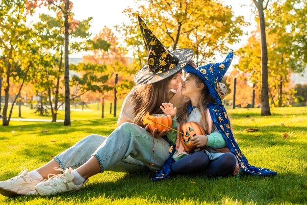 Mãe e filha em fantasias e chapéus de bruxa no parque juntos, doces ou travessuras Feliz Dia das Bruxas