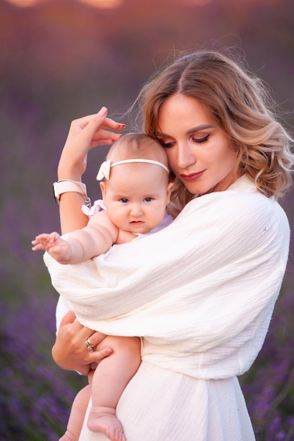 Mãe e filha em lindos vestidos brancos em um campo de lavanda no verão ao pôr do sol.