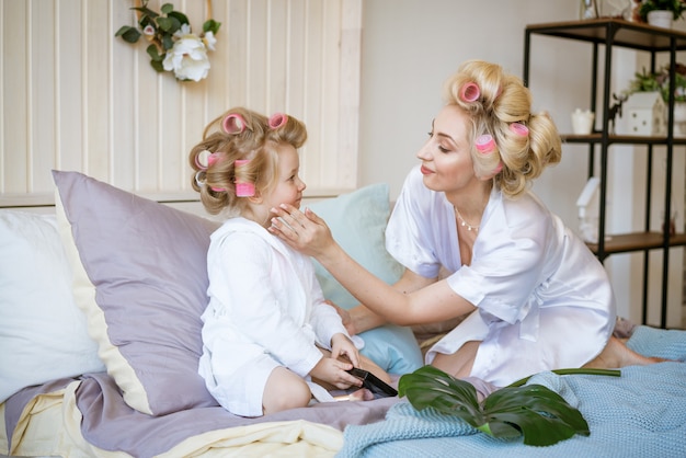 Mãe e filha em rolos e um roupão na cama