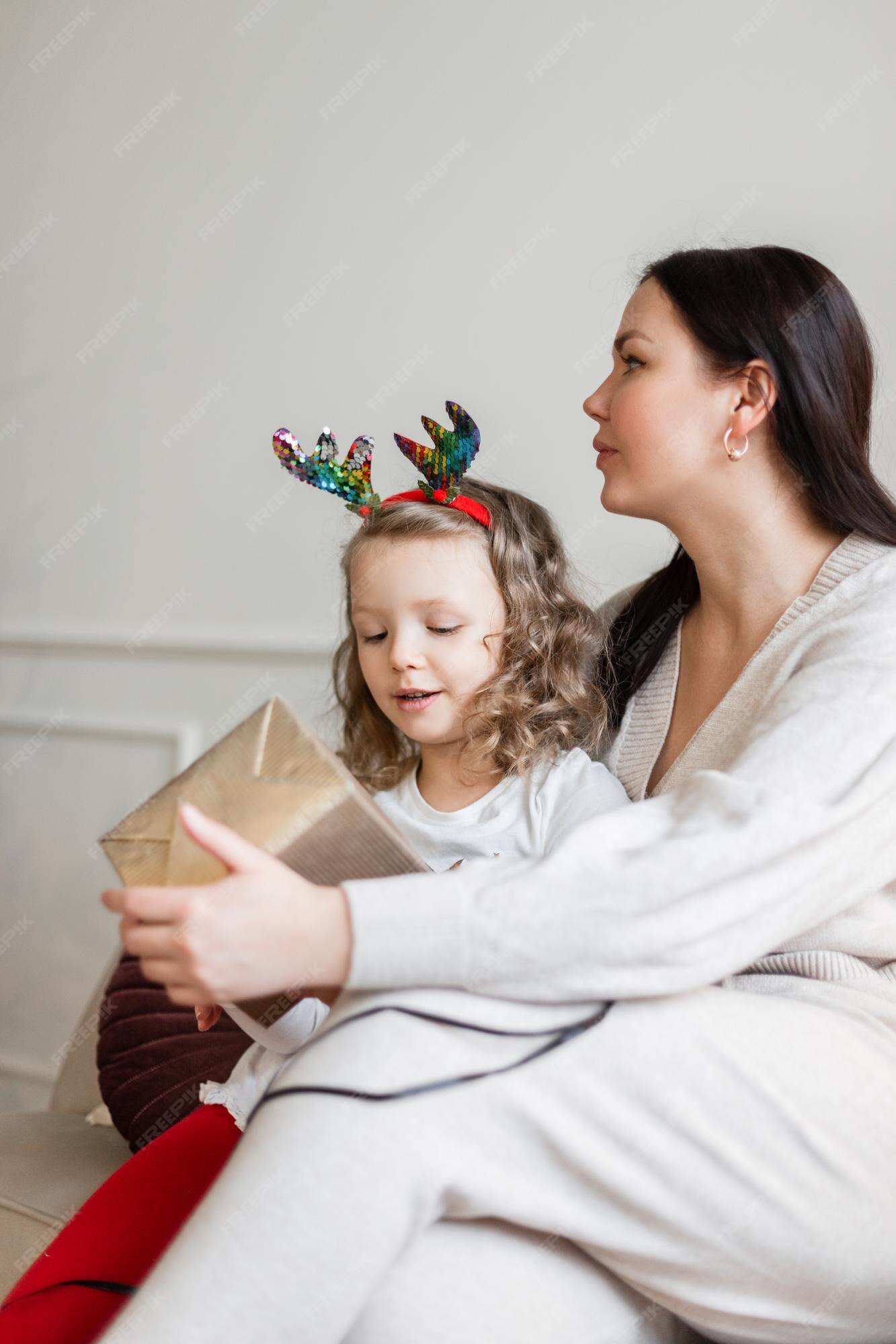 Mãe e filha em roupas da moda estão sentadas no sofá com um presente no  natal | Foto Premium