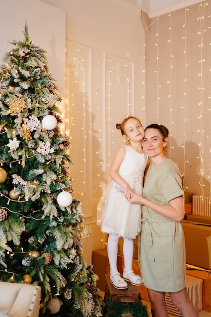 Mãe e filha em um vestido branco na árvore de natal