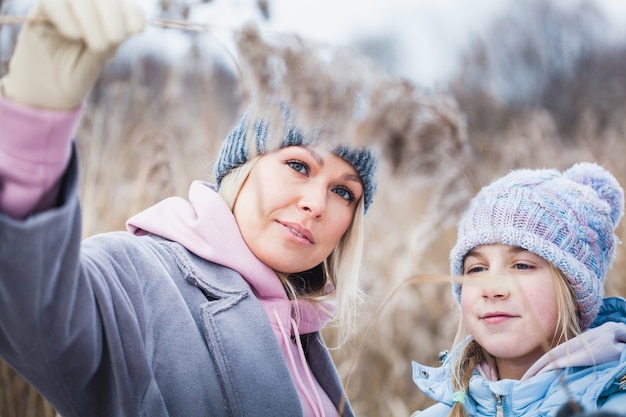 Foto mãe e filha em uma caminhada na floresta, grama e neve, caminhadas de inverno, floresta, campo, roupas de inverno
