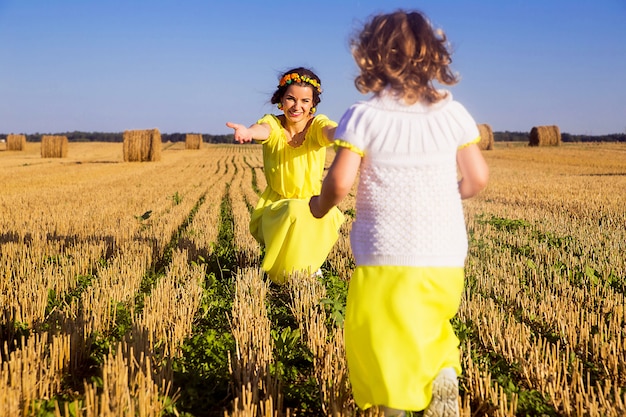 Mãe e filha em vestidos amarelos em um campo de feno