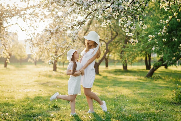 Mãe e filha em vestidos brancos se abraçam na primavera no parque