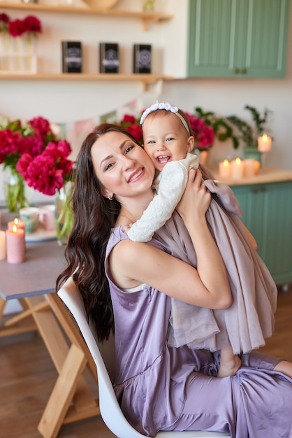 Mãe e filha em vestidos elegantes na cozinha, decorada com peônias