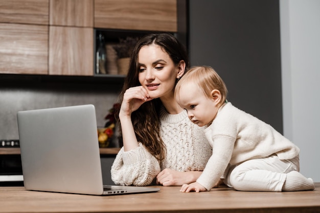 Mãe e filha estão assistindo desenhos animados no laptop em casa na cozinha Maternidade Família de mãe e filha passando tempo juntos e assistindo a vídeos online