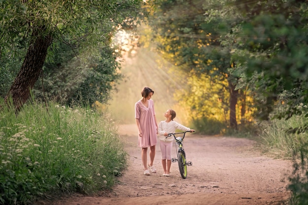 mãe e filha estão caminhando em um parque com uma bicicleta