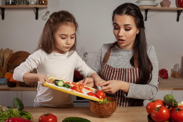 Mãe e filha estão fazendo salada de legumes e se divertindo na cozinha.