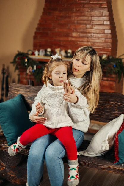 Foto mãe e filha estão lendo enquanto se divertem junto à lareira no natal ou na véspera de ano novo