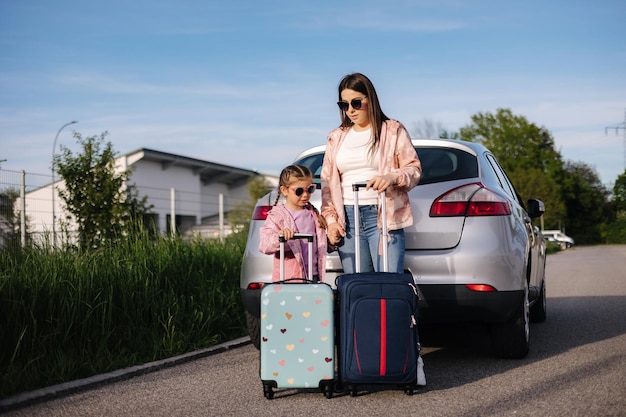 Mãe e filha estão perto do carro com suas malas e esperando a viagem de família