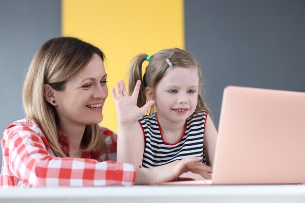 Mãe e filha estão sentadas em frente ao laptop e acenando