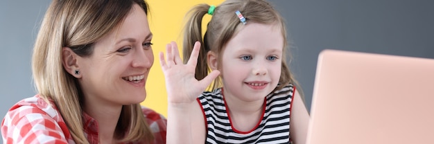 Mãe e filha estão sentadas em frente ao laptop e acenando